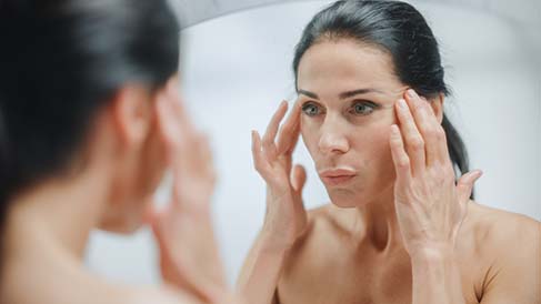 Woman looking in mirror wishing for non-surgical facelift.